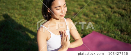 Portrait of young mindful woman, practice yoga, exercising, inhale and exhale on fresh air in park, sitting on rubber mat 108427536