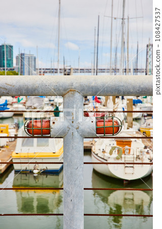 White metal railing and brown iron wires with big heavy duty red lights with blurry boats and city 108427537