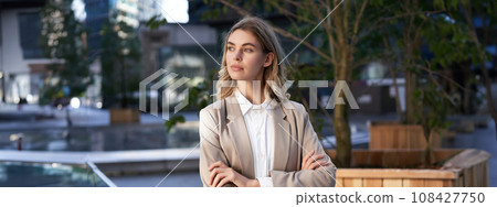 Close up portrait of confident and successful businesswoman in suit, cross arms on chest, standing in power pose on street near office building 108427750