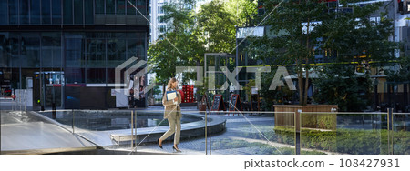 Businesswoman in suit, walking in city, going to work with laptop and documents. Corporate people concept 108427931