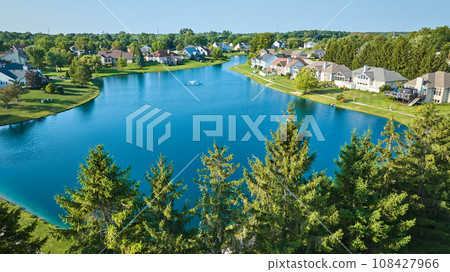 Low aerial with tree top view of large pond with water fountain and rich neighborhood on sunny day 108427966