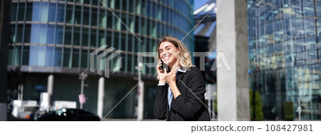 Pleased businesswoman celebrates on street, talking on mobile phone, receive good news on call Pleased businesswoman celebrates on street, talking on mobile phone, receive good news on call 108427981