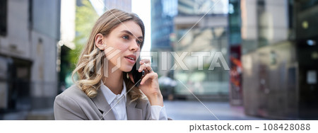 Corporate woman has conversation on phone, calling someone on mobile, wearing suit, sitting in city center Corporate woman has conversation on phone, calling someone on mobile, wearing suit, sitting in city center 108428088