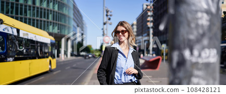 Portrait of confident corporate woman, young saleswoman in suit and sunglasses, looking self-assured on city street Portrait of confident corporate woman, young saleswoman in suit and sunglasses, looking self-assured on city street 108428121