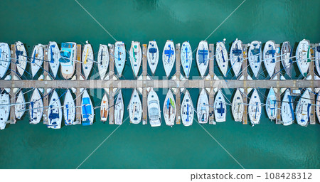 Aerial straight down view perfect row of boats on pier dock area with teal ocean water 108428312
