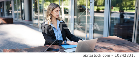 Portrait of corporate woman working on fresh air outdoors, sitting on bench with laptop, digital tablet, making notes Portrait of corporate woman working on fresh air outdoors, sitting on bench with laptop, digital tablet, making notes 108428313