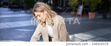 Portrait of businesswoman looks at her digital watch to check time, standing outside on street near office Portrait of businesswoman looks at her digital watch to check time, standing outside on street near office 108428374