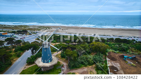 Aerial blue murphy windmill with white blades in grove of trees with sandy beach and ocean waves 108428422