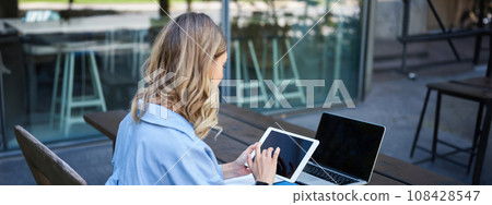 Portrait of businesswoman working on digital tablet, checking diagrams, sitting outdoors on fresh air near office building. Corporate woman prepare for work meeting 108428547