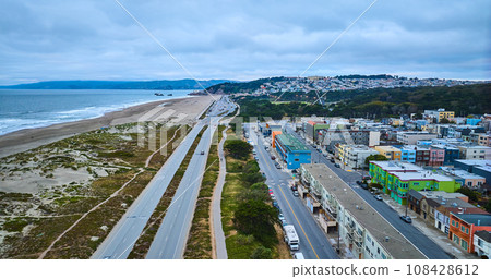 Long road split between blue sea of water with beach and two cities aerial Long road split between blue sea of water with beach and two cities aerial 108428612