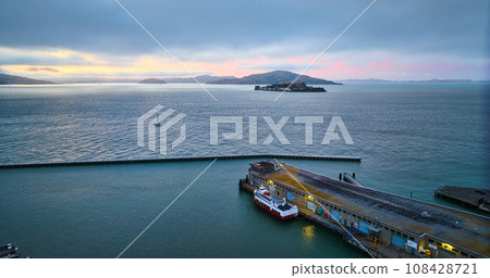 Ship at edge of pier with Alcatraz Island having pink and golden glow on horizon at dusk aerial Ship at edge of pier with Alcatraz Island having pink and golden glow on horizon at dusk aerial 108428721