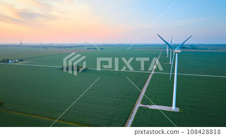 Aerial row of wind turbines in green farmland fields at sunrise or sunset with orange and pink sky 108428818