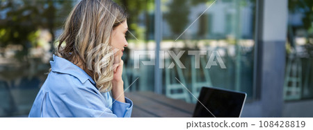 Close up portrait of woman student attend online course classes, sitting outside on fresh air with laptop and taking notes. Businesswoman video chat on computer 108428819