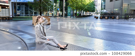 Successful businesswoman having a break, siting in city centre, looking away, adjusting her hairstyle Successful businesswoman having a break, siting in city centre, looking away, adjusting her hairstyle 108429066