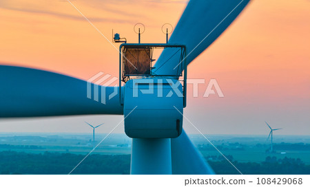 Close up of motor on wind turbine with orange sunset aerial of wind farm Close up of motor on wind turbine with orange sunset aerial of wind farm 108429068
