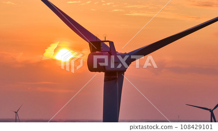 Golden sun at sunset behind close up of top of wind turbine with two distant turbines aerial 108429101