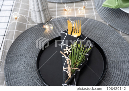 Serving a festive table with plates, forks, knives, napkins close-up tissue in a cage decorated for Christmas and New Year pine branch with a cone. Eco-style, minimalism Serving a festive table with plates, forks, knives, napkins close-up tissue in a cage decorated for Christmas and New Year pine branch with a cone. Eco-style, minimalism 108429142