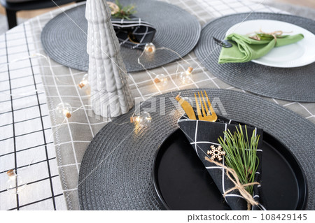 Serving a festive table with plates, forks, knives, napkins close-up tissue in a cage decorated for Christmas and New Year pine branch with a cone. Eco-style, minimalism 108429145
