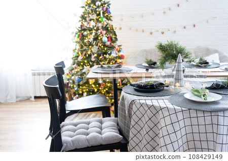 Serving a festive table with plates, forks, knives, napkins, glasses close-up in the modern interior of a loft house decorated for Christmas and New Year. Waiting for guests for a festive dinner 108429149