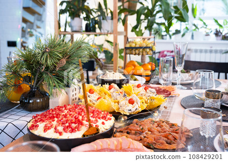 Serving a festive table with snacks, salads and goodies close-up in the modern interior of a loft house decorated for Christmas and New Year. Waiting for guests for a festive dinner Serving a festive table with snacks, salads and goodies close-up in the modern interior of a loft house decorated for Christmas and New Year. Waiting for guests for a festive dinner 108429201