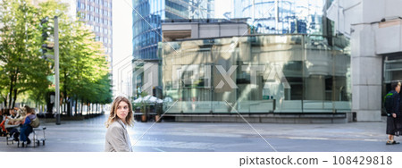 Female corporate worker sitting outdoors near office buildings, turn back and look behind, waiting for coworker on lunch break Female corporate worker sitting outdoors near office buildings, turn back and look behind, waiting for coworker on lunch break 108429818