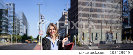 Portrait of successful young company ceo, businesswoman in black suit, standing on sunny street and smiling Portrait of successful young company ceo, businesswoman in black suit, standing on sunny street and smiling 108429949
