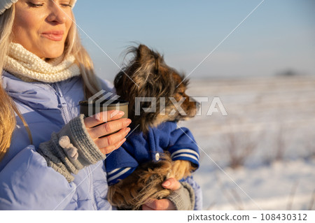 A blonde woman carries a small dog in her arms. 108430312