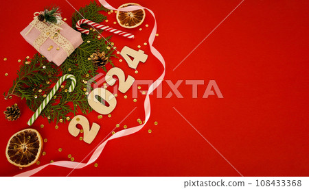 Christmas frame with a branches of thuja and gifts on a red background. Winter holidays. Space for text. Top view, flat lay. Christmas. Template, layout. A greeting card with numers 2024 Christmas frame with a branches of thuja and gifts on a red background. Winter holidays. Space for text. Top view, flat lay. Christmas. Template, layout. A greeting card with numers 2024 108433368