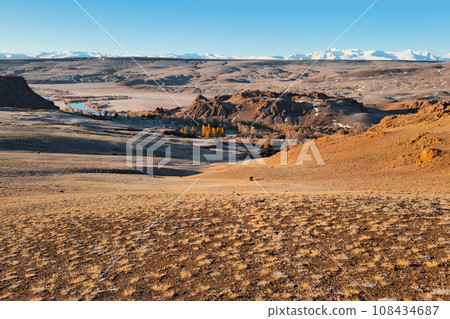 Bright autumn mountain steppe landscape. Awesome alpine view from pass to mountain valley in sunlight and great mountain silhouettes on horizon. Altai region. Bright autumn mountain steppe landscape. Awesome alpine view from pass to mountain valley in sunlight and great mountain silhouettes on horizon. Altai region. 108434687
