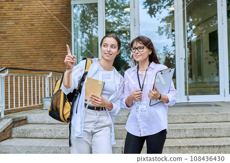 Teenage girl student talking to female teacher, standing on steps of educational building Teenage girl student talking to female teacher, standing on steps of educational building 108436430