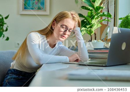 Sad pensive young teenage girl sitting near smartphone laptop at home. 108436453