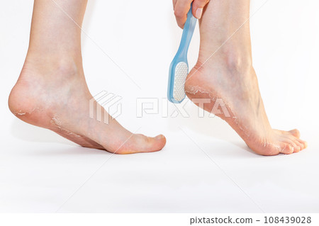 Side view of female legs, with pumice rubbing peeling skin of soles on heels. Close up. White background. Skin care and pedicure 108439028