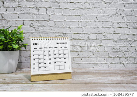 White December 2024 calendar on office wooden desk with potted plant. 108439577