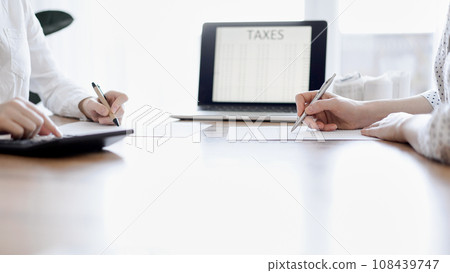 Two accountants using a laptop computer and calculator while counting taxes at wooden desk in office. Teamwork in business audit and finance 108439747