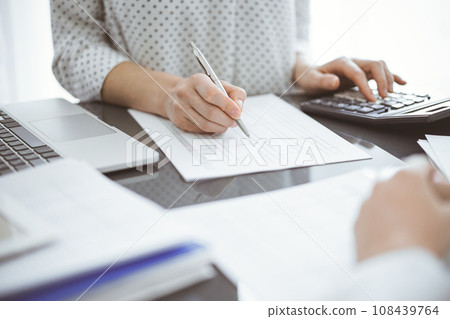 Woman accountant using a calculator and laptop computer while counting taxes for a client. Business audit concepts 108439764