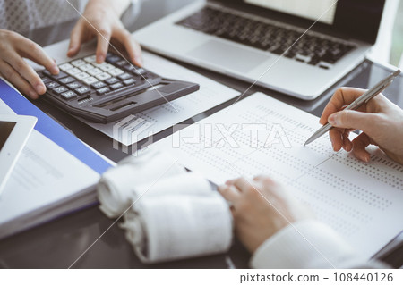 Woman accountant using a calculator and laptop computer while counting taxes for a client. Business audit concepts Woman accountant using a calculator and laptop computer while counting taxes for a client. Business audit concepts 108440126