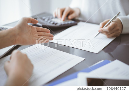 Woman accountant using a calculator and laptop computer while counting and discussing taxes with a client. Business audit concepts Woman accountant using a calculator and laptop computer while counting and discussing taxes with a client. Business audit concepts 108440127