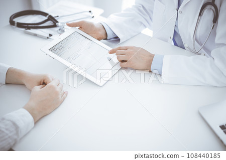 Doctor and patient sitting opposite each other at the desk in clinic. The focus is on female physician's hands pointing into tablet computer touchpad, close up. Medicine concept Doctor and patient sitting opposite each other at the desk in clinic. The focus is on female physician's hands pointing into tablet computer touchpad, close up. Medicine concept 108440185