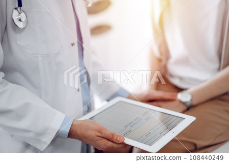 Doctor and patient discussing health exam results. Friendly physician reassuring a young woman by one hand while keeping tablet computer in another. Medicine concept Doctor and patient discussing health exam results. Friendly physician reassuring a young woman by one hand while keeping tablet computer in another. Medicine concept 108440249