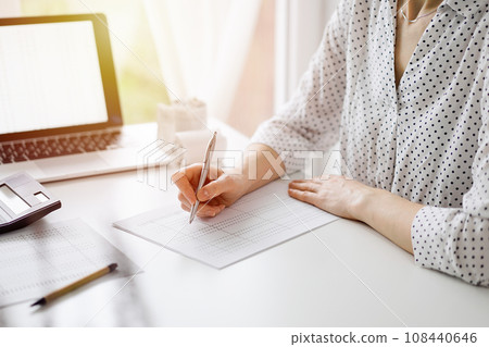 Woman accountant using a calculator and laptop computer while counting taxes at the white table in office. Business audit and finance concepts Woman accountant using a calculator and laptop computer while counting taxes at the white table in office. Business audit and finance concepts 108440646