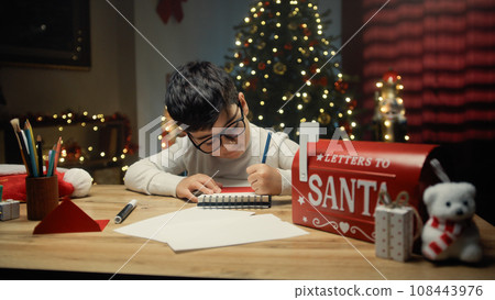 Kid writing Christmas letter on his notebook  108443976