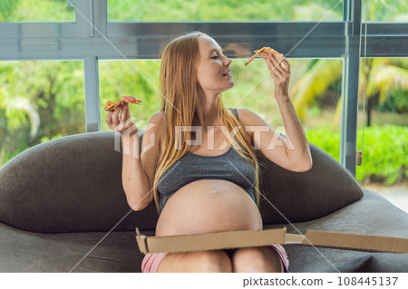 A pregnant woman enjoys a slice of pizza, savoring a moment of indulgence while satisfying her craving for a delightful, comforting treat. Excited Pregnant Young Lady Enjoying Pizza Holding Biting 108445137