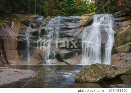 Mumlava waterfall, in the foreground granite stone. Mountain river Mumlava, Krkonose national park, Czech Republic, summer afternoon. Mumlava waterfall, in the foreground granite stone. Mountain river Mumlava, Krkonose national park, Czech Republic, summer afternoon. 108445261