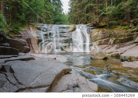 Mumlava waterfall, in the foreground right stone riverside. Mountain river Mumlava, Krkonose national park, Czech Republic, summer afternoon. Mumlava waterfall, in the foreground right stone riverside. Mountain river Mumlava, Krkonose national park, Czech Republic, summer afternoon. 108445269