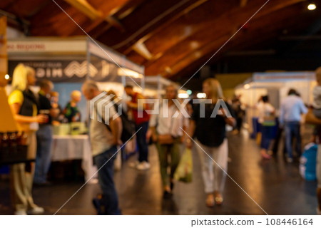 Dark blurry shot of people at the exhibition. People walk around, try different things and shop. 108446164