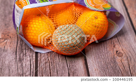 Within a mesh bag containing oranges, there is a single orange that has gone bad and developed mold. 108446195