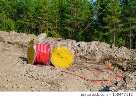 Wooden Reel with High Voltage Red Cable in Forest: Ready for Underground Power Line Installation Wooden Reel with High Voltage Red Cable in Forest: Ready for Underground Power Line Installation 108447118