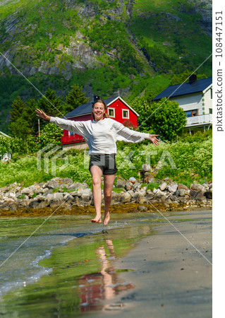 Young girl teenager running on beach in Norway Fjord. Vacation in Nordland in summer 108447151