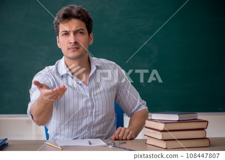 Young male teacher in front of green board 108447807