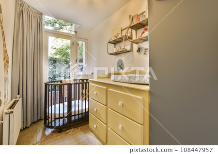 a baby's room with a cribt in the corner and an open door leading to another room 108447957